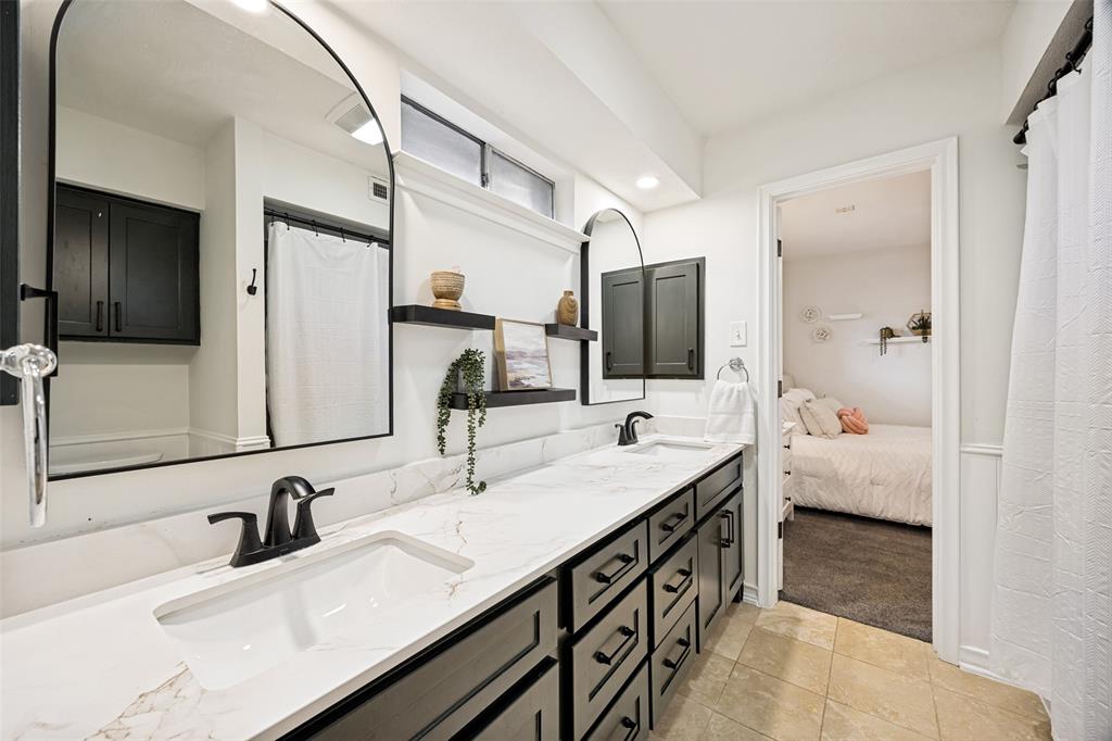 3151 Merrell Road Dallas, TX 75229 - Photo 19 of 25 Dual-sink vanity featuring a white countertop with integrated sinks, matte black faucets, and dark wood-finish cabinetry