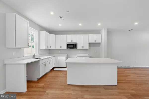 a large kitchen with stainless steel appliances granite countertop a stove a sink a refrigerator and white cabinets with wooden floor