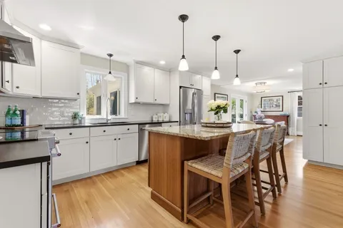 a kitchen with stainless steel appliances granite countertop a kitchen island a stove a refrigerator a sink a dining table and chairs with wooden floor