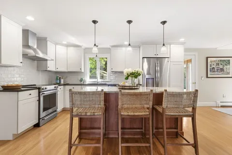 a kitchen with stainless steel appliances granite countertop a stove top oven a refrigerator a sink and chairs
