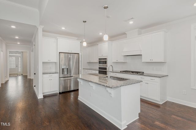 a kitchen with stainless steel appliances granite countertop a sink a stove a refrigerator and island with wooden floor