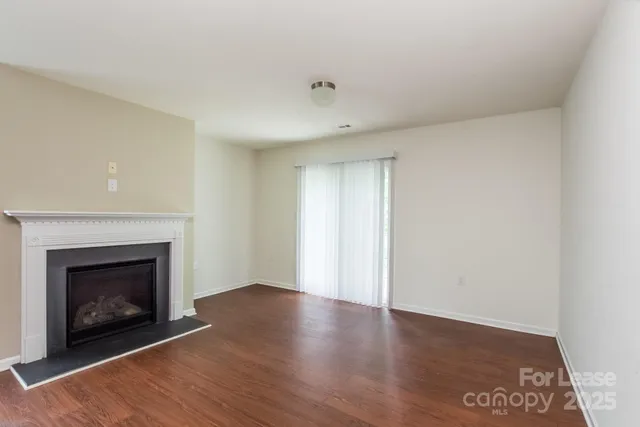 a view of an empty room with wooden floor fireplace and a window