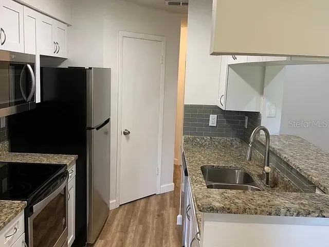 a kitchen with stainless steel appliances granite countertop a refrigerator a stove and a sink with wooden floor