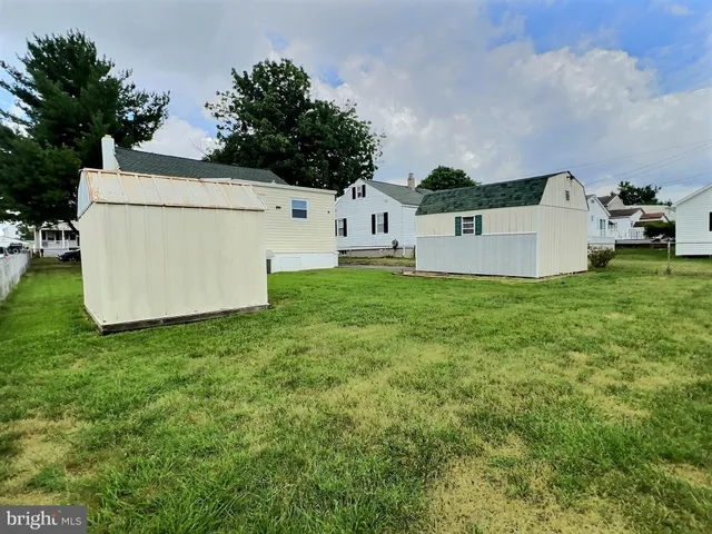 a view of a white house in front of a big yard with plants and large tree