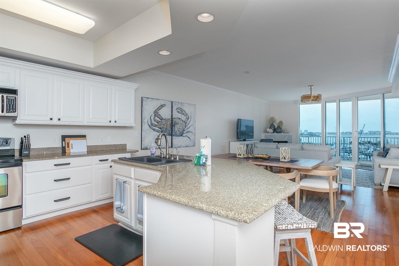 27800 Canal Road, Unit 411 Orange Beach, AL 36561 - Photo 10 of 49 Open-concept kitchen featuring an island with a countertop extension, white cabinetry with dark hardware, stainless steel appliances, and wood-finish flooring