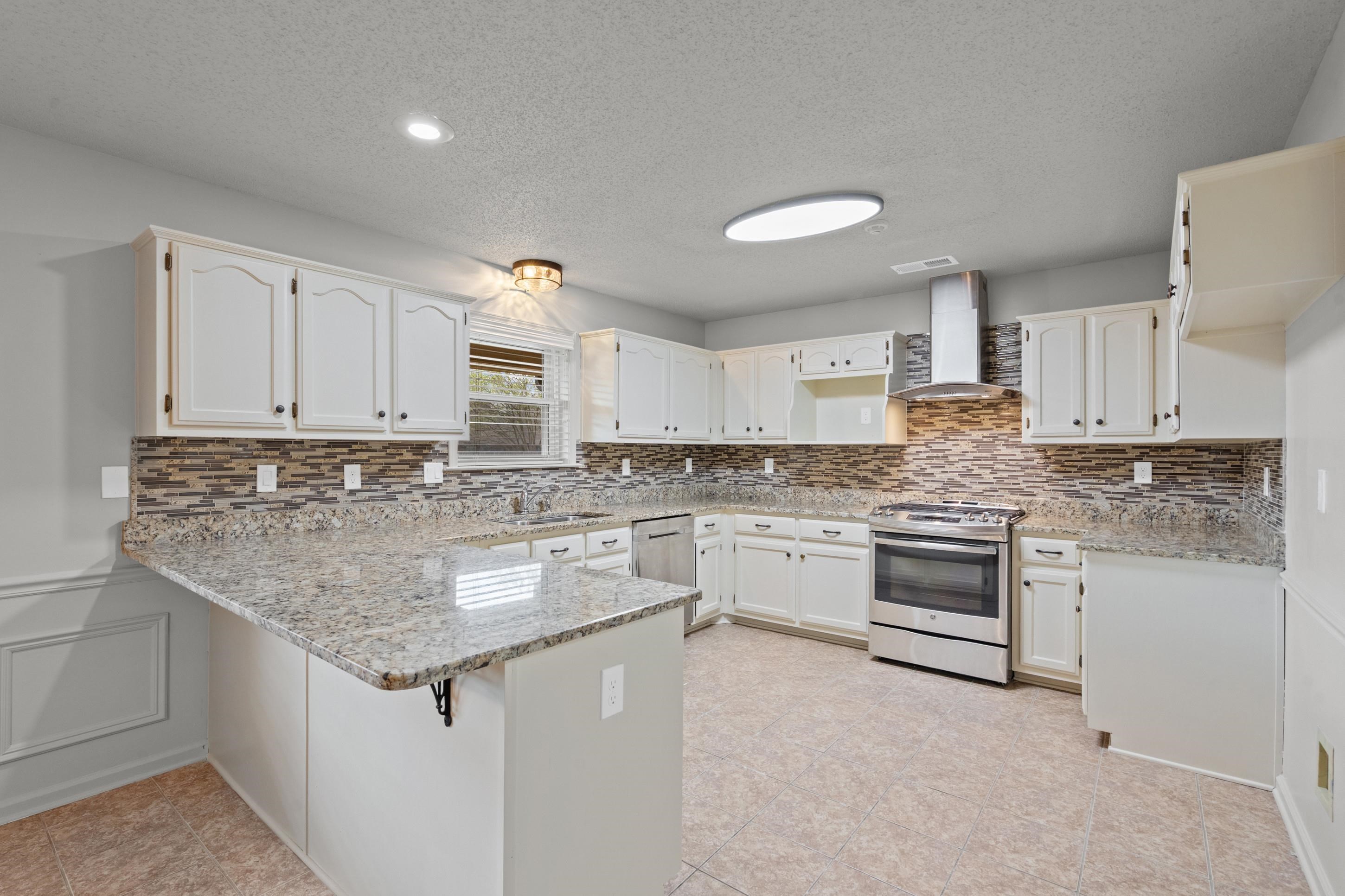 1301 Wolf Lair Drive Collierville, TN 38017 - Photo 4 of 32 Kitchen featuring a peninsula, light stone counters, stainless steel appliances, a breakfast bar area, and white cabinets