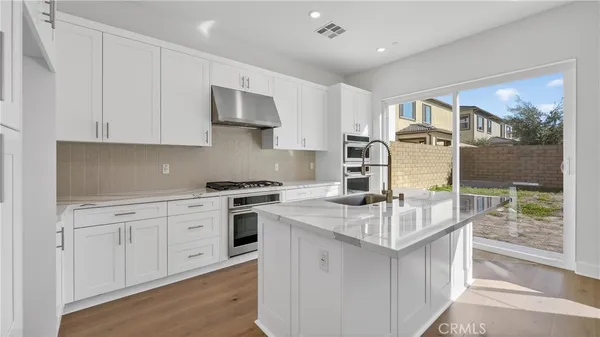 a kitchen with stainless steel appliances granite countertop a stove top oven a sink dishwasher and white cabinets with wooden floor