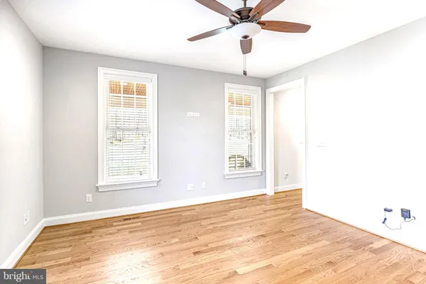 an empty room with wooden floor chandelier fan and windows
