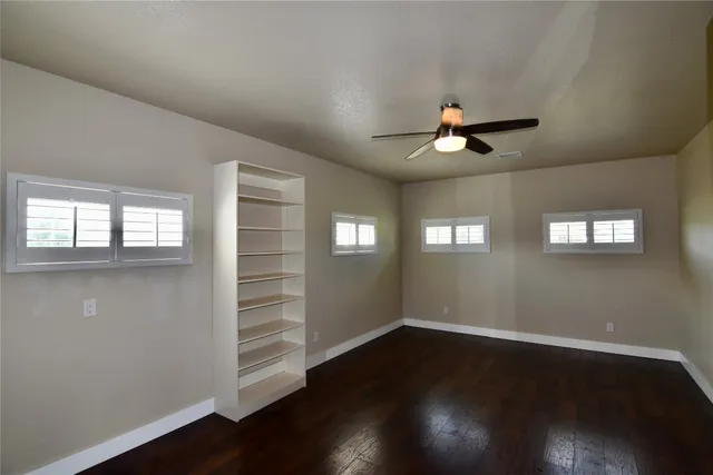 an empty room with wooden floor chandelier fan and windows