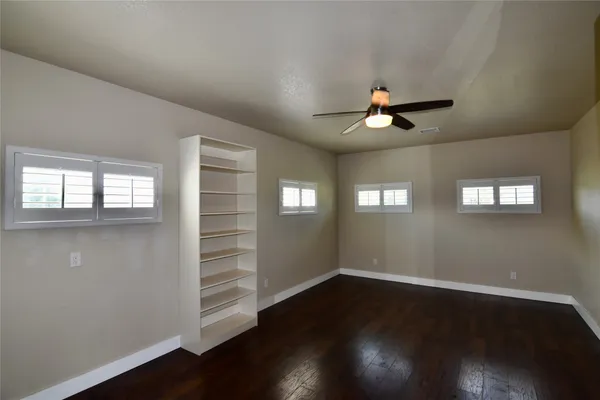 a view of an empty room with wooden floor and a ceiling fan