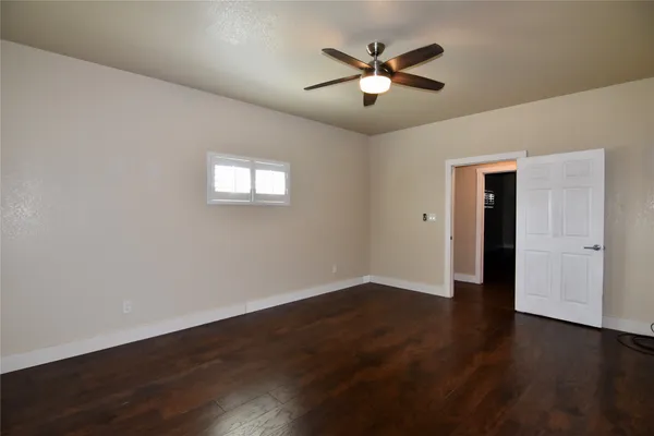 a view of an empty room with wooden floor and a ceiling fan