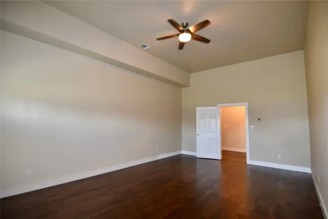 a view of an empty room with wooden floor and a ceiling fan