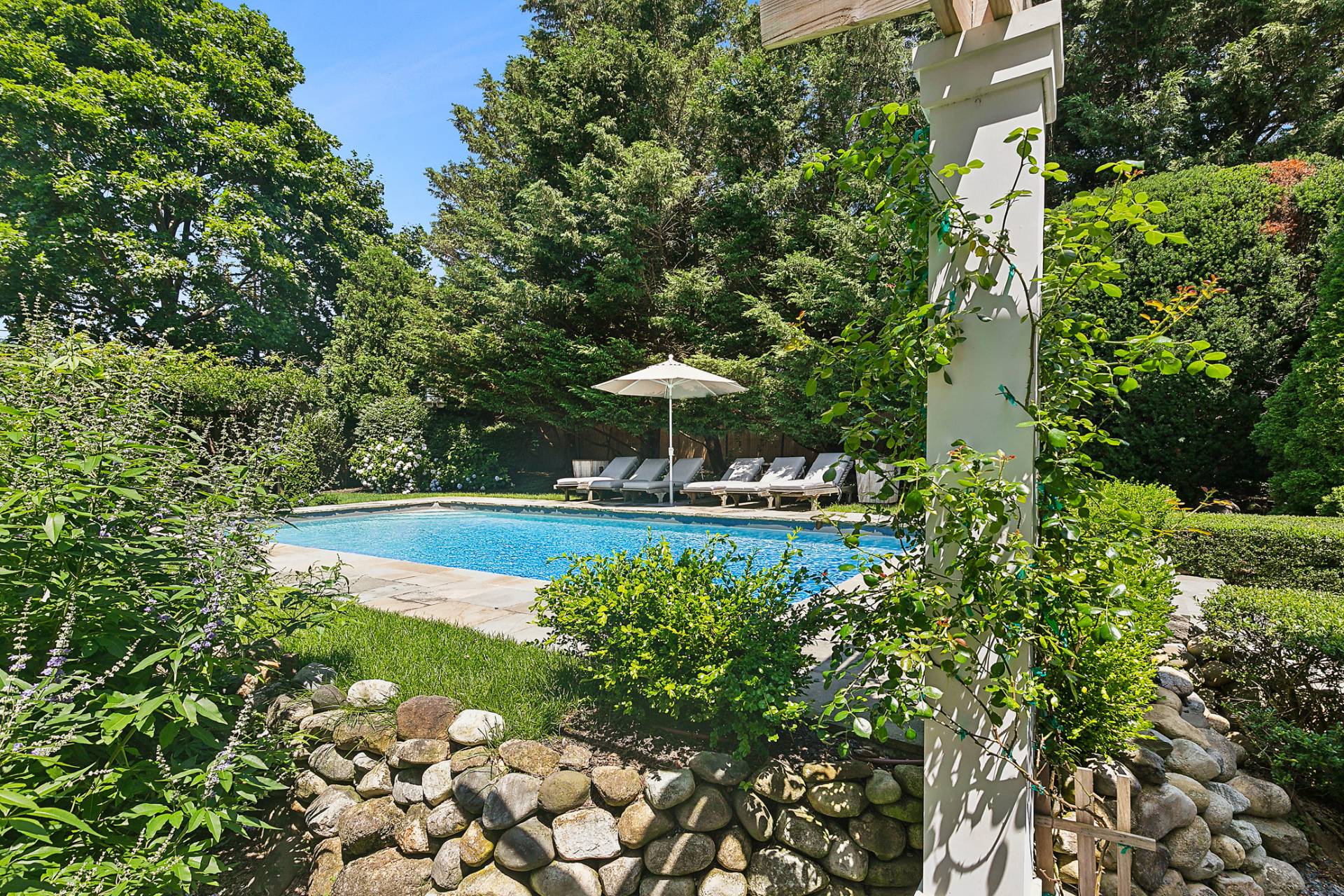 35 Harris Lane Southampton, NY 11968 - Photo 5 of 17 a view of a swimming pool with a bench and trees in the background