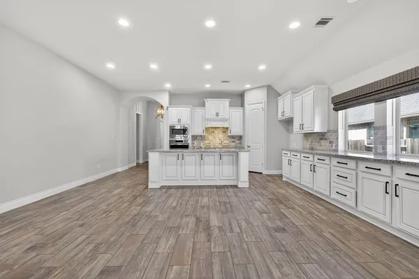 a large kitchen with stainless steel appliances a large counter top a stove a sink cabinets and a wooden floor