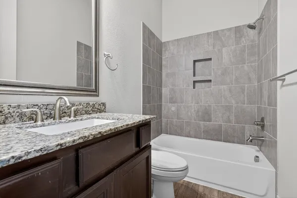 a bathroom with a granite countertop bathtub sink vanity mirror and toilet