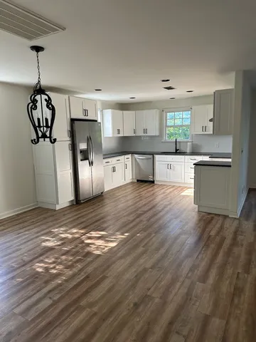 a kitchen with stainless steel appliances granite countertop a refrigerator a sink dishwasher a stove and white cabinets with wooden floor