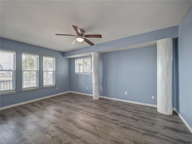 an empty room with wooden floor fan and windows