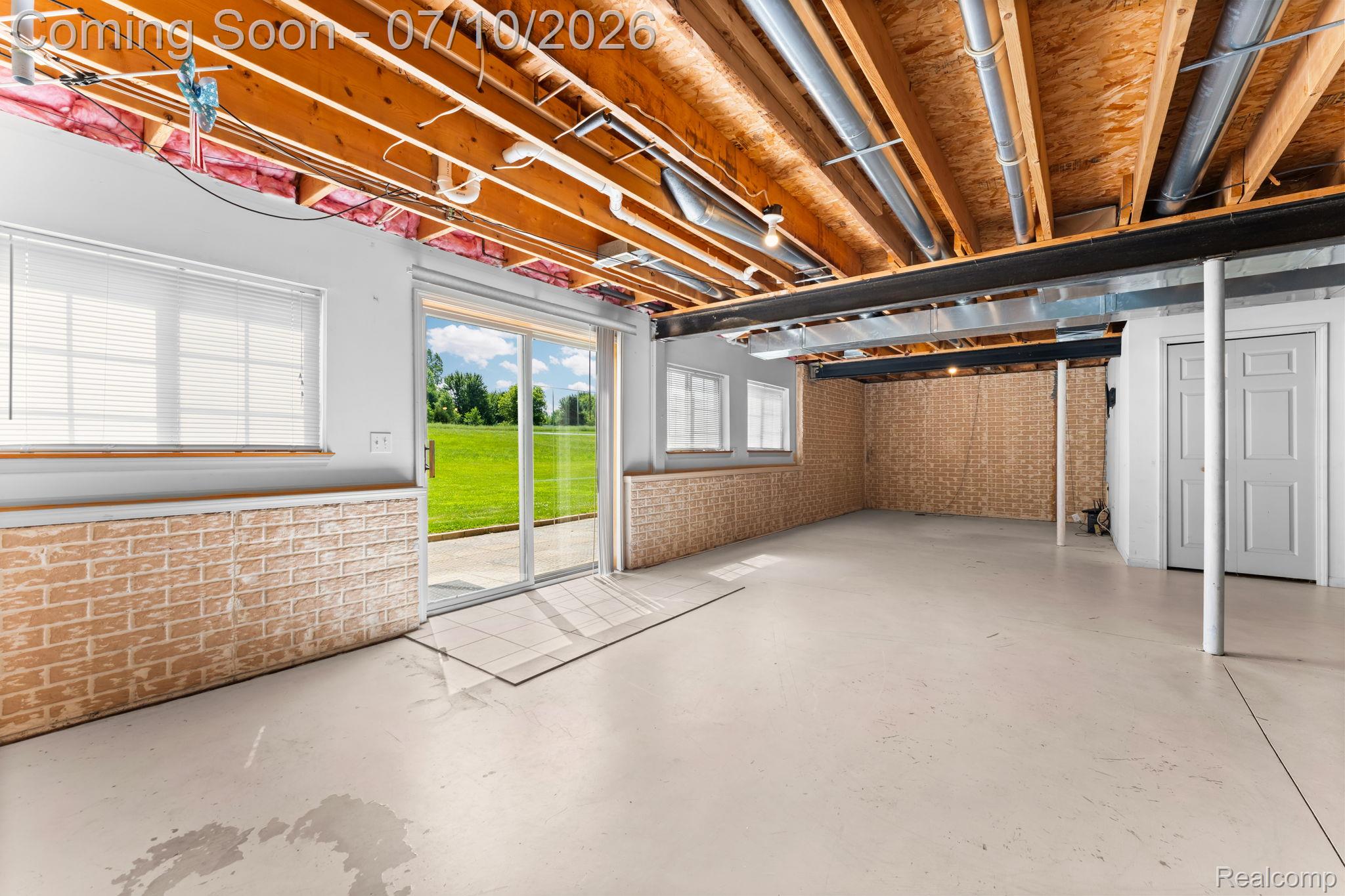 3144 North Nicholson Road Fowlerville, MI 48836 - Photo 65 of 70 Walk-out lower level featuring exposed wood joists, a sliding glass door, multiple windows with blinds, light-colored concrete flooring, and an open layout