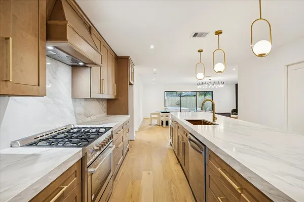 a large kitchen with stainless steel appliances granite countertop a stove a sink dishwasher and white cabinets with wooden floor