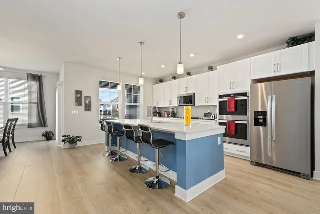 a kitchen with stainless steel appliances a stove a sink a refrigerator white cabinets and wooden floor