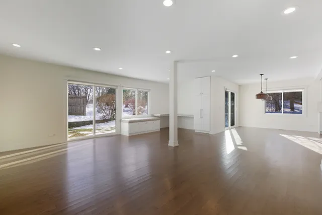 a view of an empty room with wooden floor and kitchen view