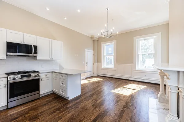 a kitchen with stainless steel appliances granite countertop a stove top oven a sink dishwasher a refrigerator and a dining table with wooden floor
