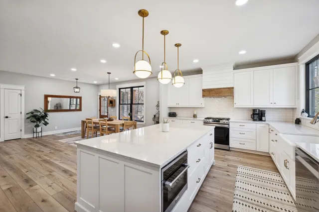a large white kitchen with a stove a sink a kitchen island with chairs and wooden floor