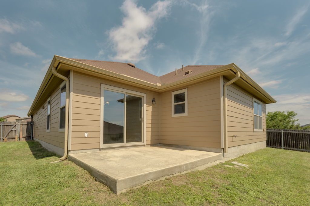 210 Cushman Drive Kyle, TX 78640 - Photo 2 of 21 Rear exterior featuring a concrete patio, sliding glass door, tan horizontal siding, and a brown shingle roof