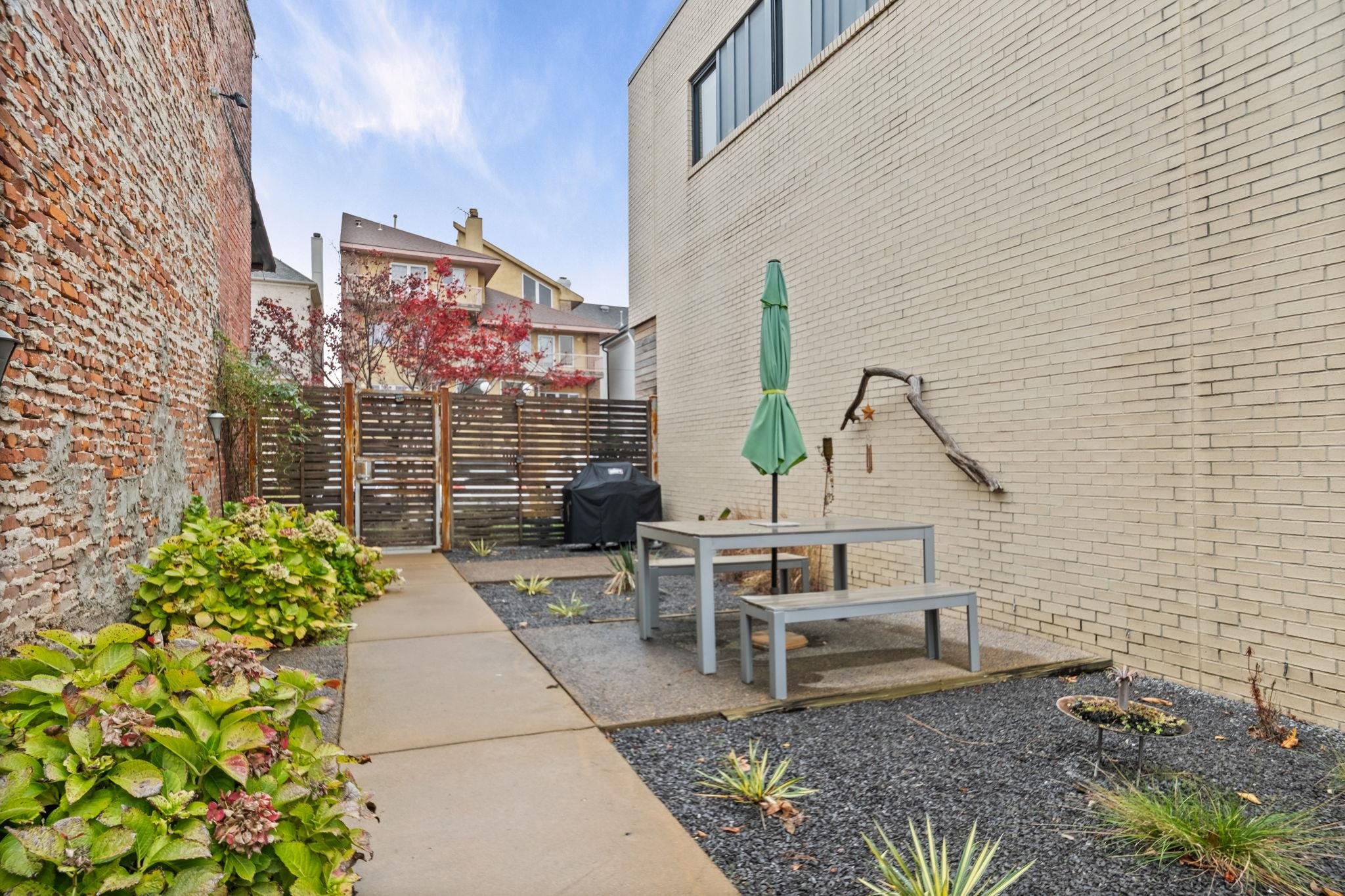 448 Tennessee Street Memphis, TN 38103 - Photo 11 of 39 Private outdoor patio featuring a concrete paver path, dark gravel landscaping, mature shrubs, and a slatted privacy fence