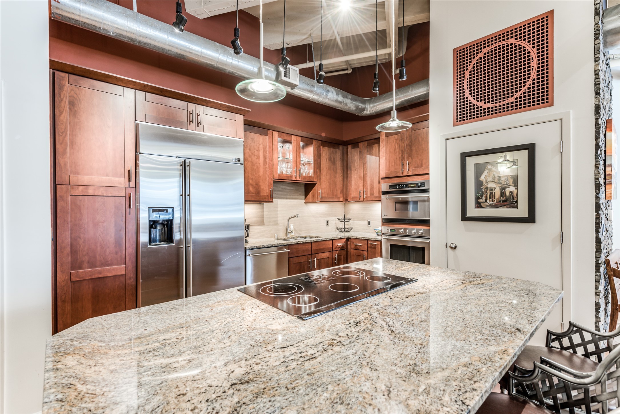 705 Main Street, Unit 215 Houston, TX 77002 - Photo 3 of 36 Modern kitchen with stainless steel appliances, granite countertops, and rich wooden cabinetry. Features an island with a built-in cooktop and industrial-style lighting, offering a stylish and functional space.