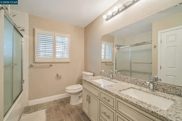 a bathroom with a granite countertop double vanity sink a mirror and a toilet
