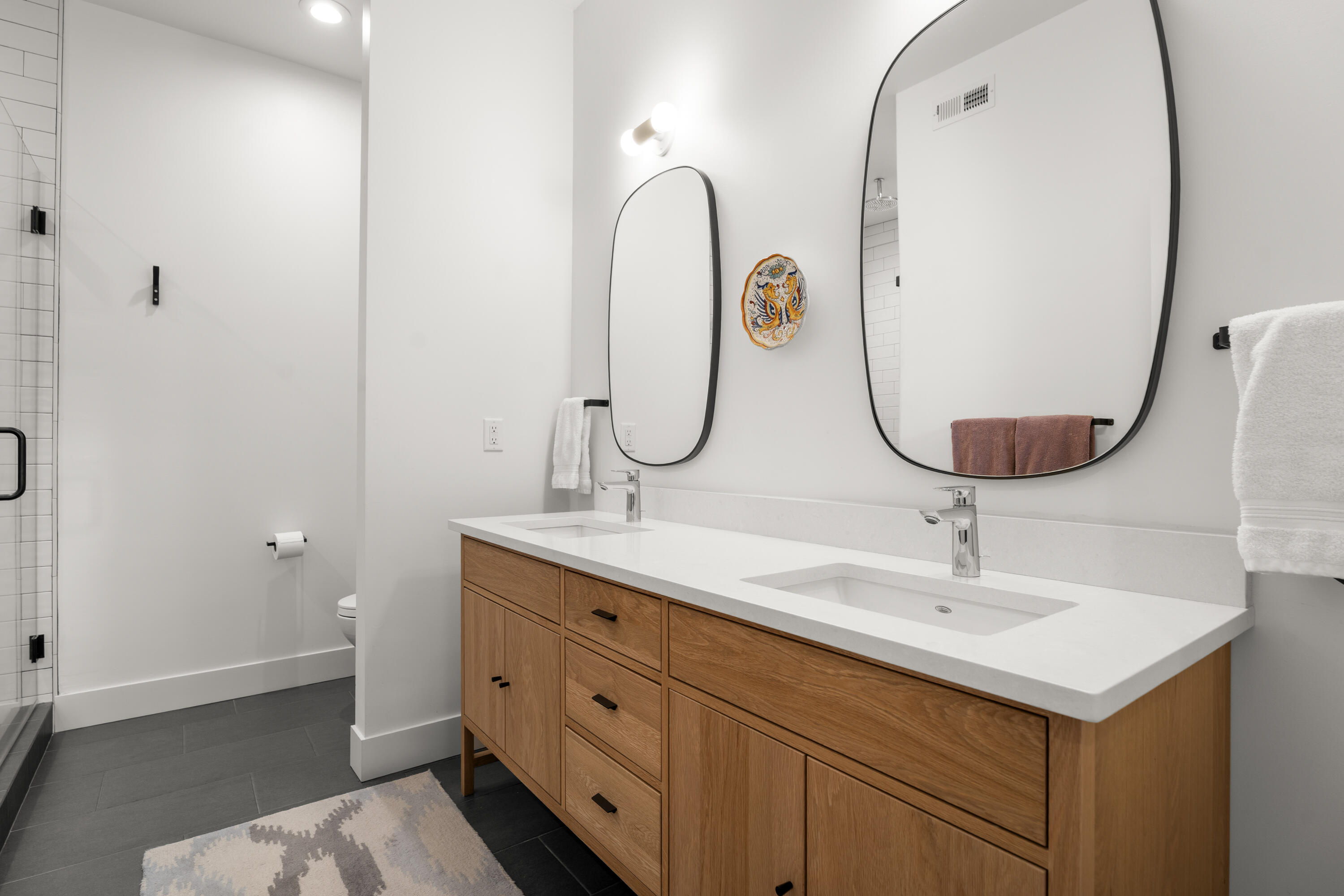 56670 Sunstone Loop, Unit LOT 141 Bend, OR 97707 - Photo 18 of 62 Bright ensuite bath with dual white oak vanities, quartz countertop, oversized mirrors, and a spacious tiled walk-in shower with bench and niche storage.