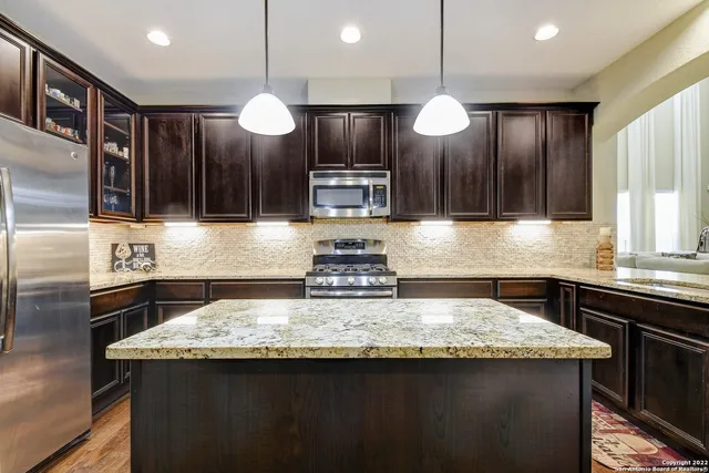 a kitchen with kitchen island granite countertop stainless steel appliances a counter space a sink and a refrigerator