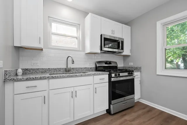 a kitchen with stainless steel appliances granite countertop white cabinets a sink a stove a microwave and window