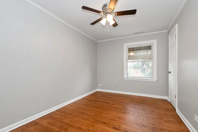 an empty room with wooden floor ceiling fan and windows