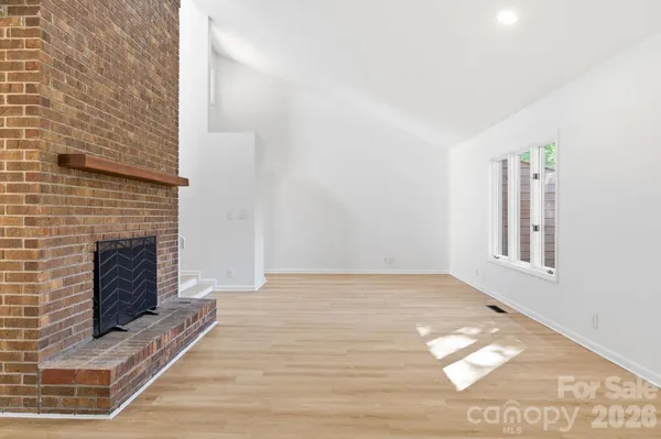 a view of an empty room with wooden floor and a fireplace