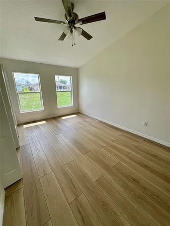an empty room with wooden floor ceiling fan and windows