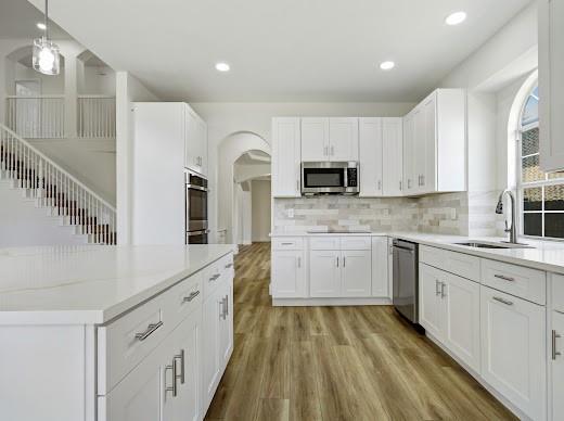 5034 West Fall Drive Midlothian, TX 76065 - Photo 15 of 40 Modern kitchen featuring white cabinetry, stainless steel appliances, a tile backsplash, light-toned countertops, and wood-finish flooring