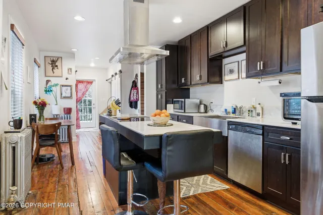 a kitchen with stainless steel appliances granite countertop a refrigerator a sink dishwasher a stove and a dining table with wooden floor