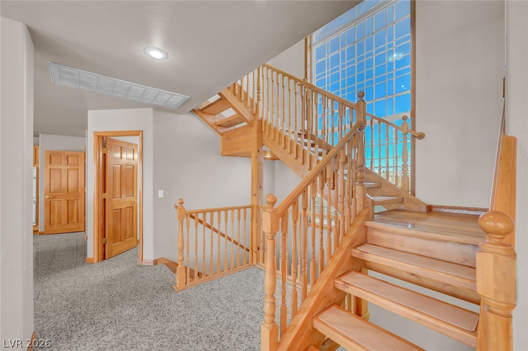 640 North Racetrack Road Henderson, NV 89015 - Photo 31 of 65 A grand wooden staircase with intricate balusters ascends to an upper level, illuminated by a tall window.