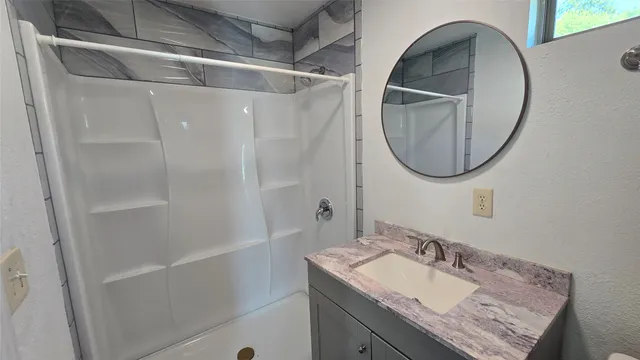 a bathroom with a granite countertop sink a mirror and shower