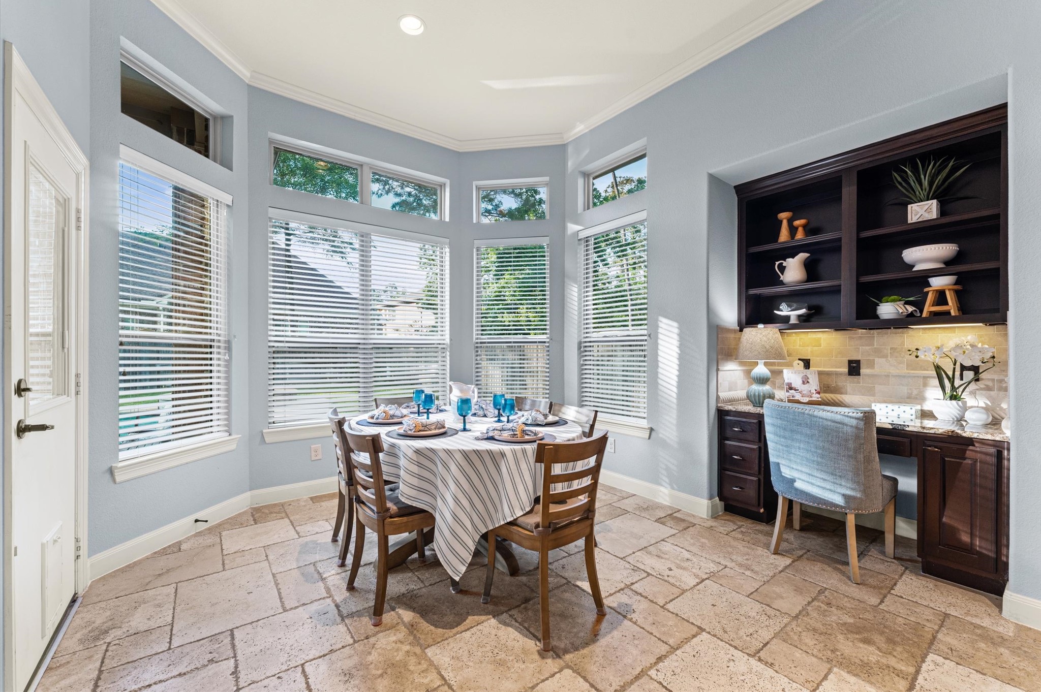 70 Valera Ridge Drive Spring, TX 77389 - Photo 19 of 37 This bright breakfast nook features large windows with blinds, offering plenty of natural light. It includes a cozy dining area and a built-in desk with shelving, perfect for a small home office or study space. The tile flooring and soft wall colors add a touch of elegance.