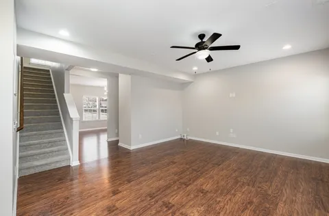a view of an empty room with wooden floor and a ceiling fan