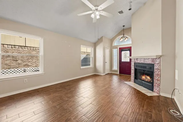 an empty room with windows a fireplace a ceiling fan and wooden floor