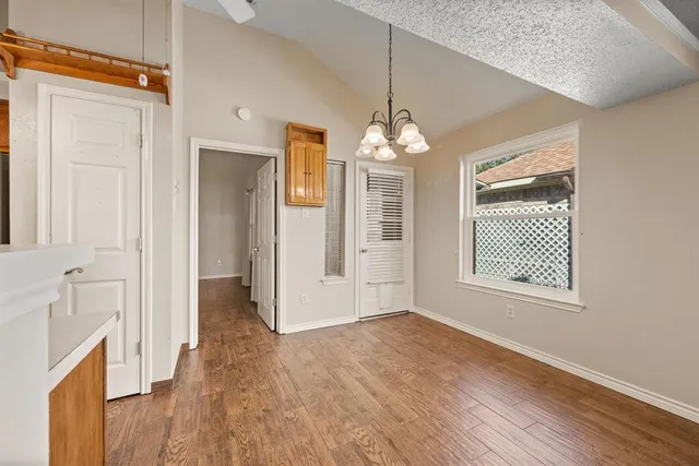 an empty room with wooden floor chandelier and windows