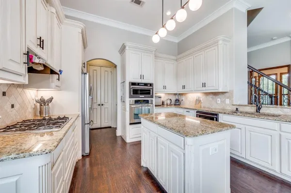 a kitchen with stainless steel appliances granite countertop a stove top oven a sink dishwasher and a refrigerator with wooden floor