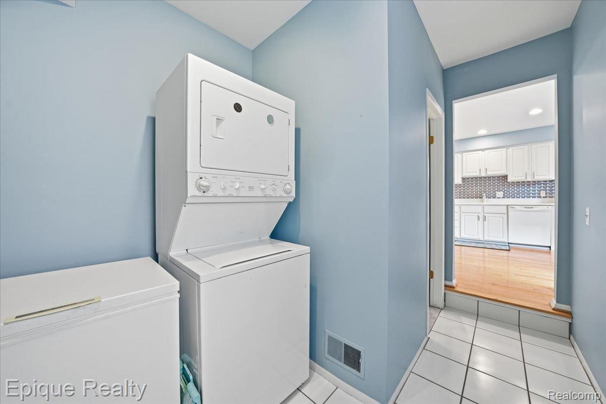 26 Kirks Court Rochester, MI 48309 - Photo 37 of 44 Dedicated laundry space featuring a white stackable washer and dryer unit, white floor tiling, and a chest freezer
