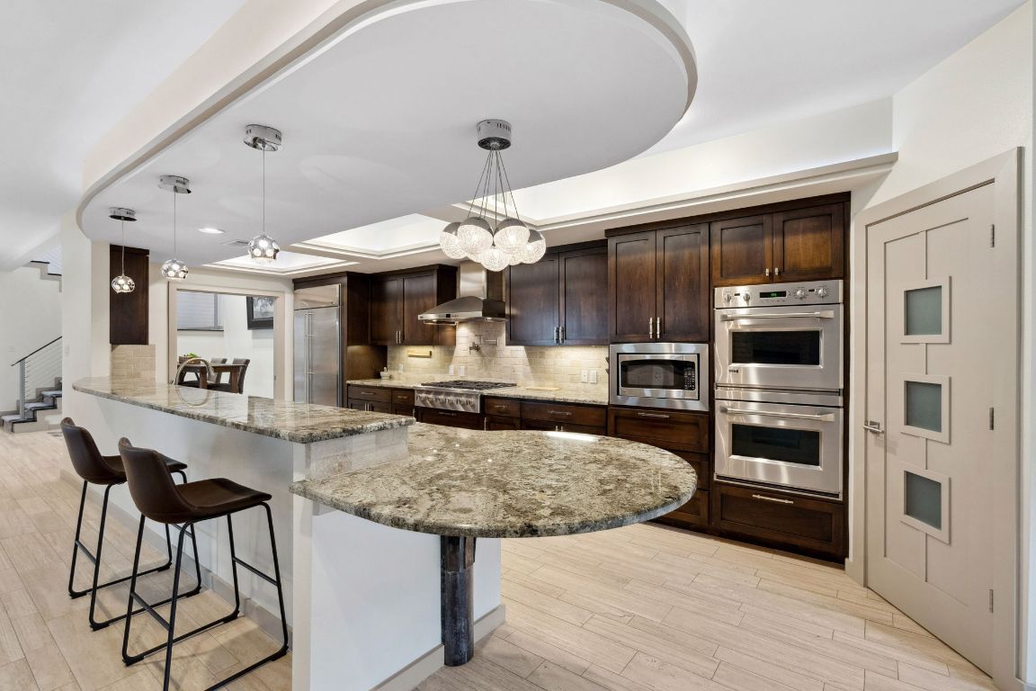 9 Swiftwater Trail The Hills, TX 78738 - Photo 12 of 34 Kitchen with decorative backsplash, pendant lighting, light stone counters, built in appliances, and a kitchen bar
