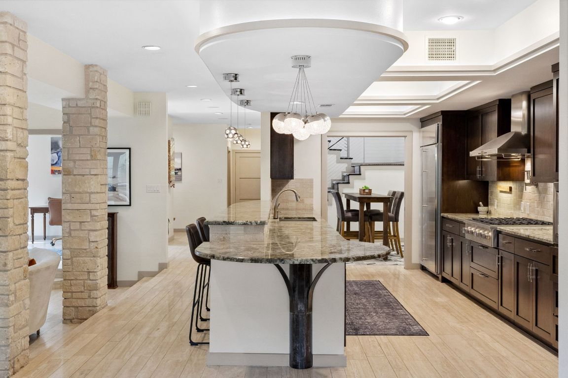 9 Swiftwater Trail The Hills, TX 78738 - Photo 13 of 34 Kitchen featuring light stone counters, backsplash, a breakfast bar, pendant lighting, and light wood-type flooring