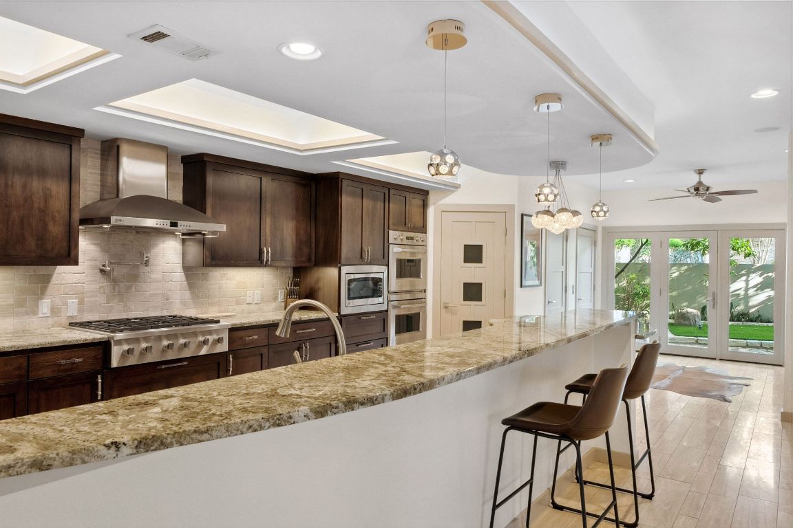 9 Swiftwater Trail The Hills, TX 78738 - Photo 15 of 34 Kitchen featuring dark brown cabinets, pendant lighting, decorative backsplash, wall chimney range hood, and light stone countertops